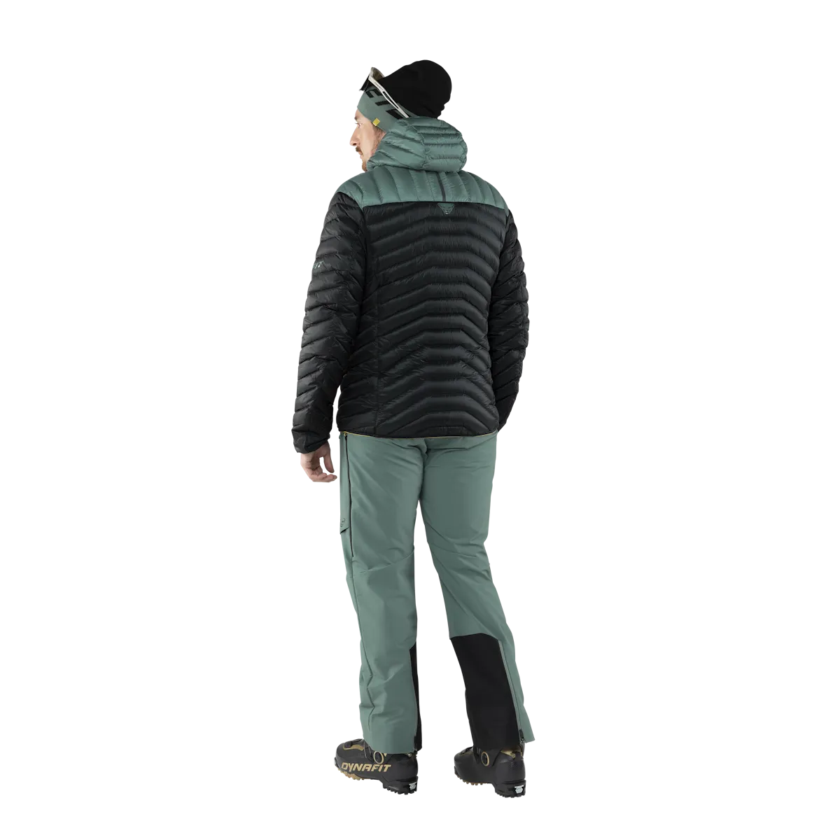 Vista posteriore: persona con piumino Dynafit Ridge Ultralight in nero e verde. Pantaloni da sci, cappello e scarponi da sci.