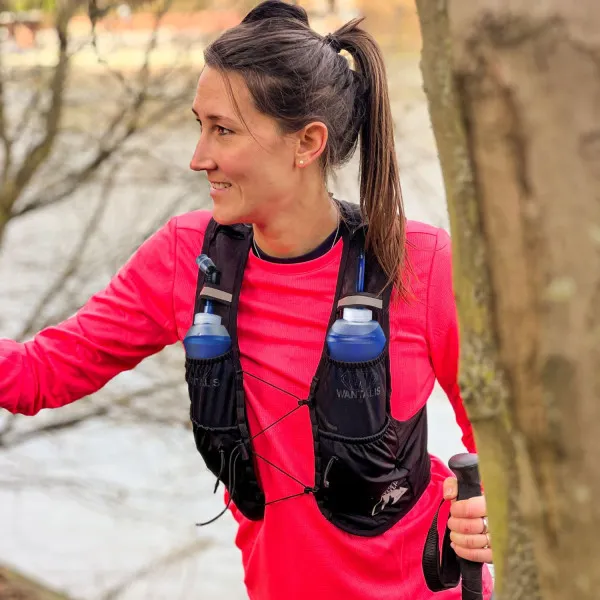 Coureuse avec gilet d'hydratation Hydrabag Elite 8L et deux gourdes bleues. Elle tient un bâton de trekking dans la main.
