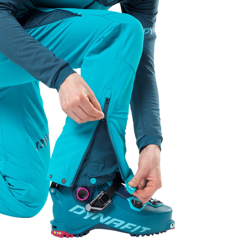 Une personne ferme la fermeture éclair de son pantalon de ski turquoise sur sa chaussure de ski turquoise Dynafit Radical Pro W.