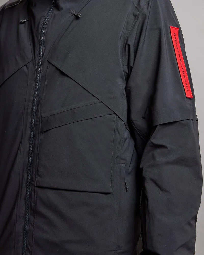 Detailaufnahme einer schwarzen S-1 Gore-Tex 2L Stretch Insulated Jacket. Sichtbar sind Taschen, Reißverschluss und Ärmel mit rotem Logo.