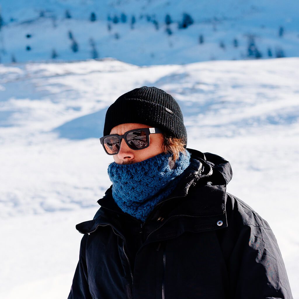 Mann mit Mütze, Sonnenbrille und blauem Stroller Neckwarmer im Schnee.