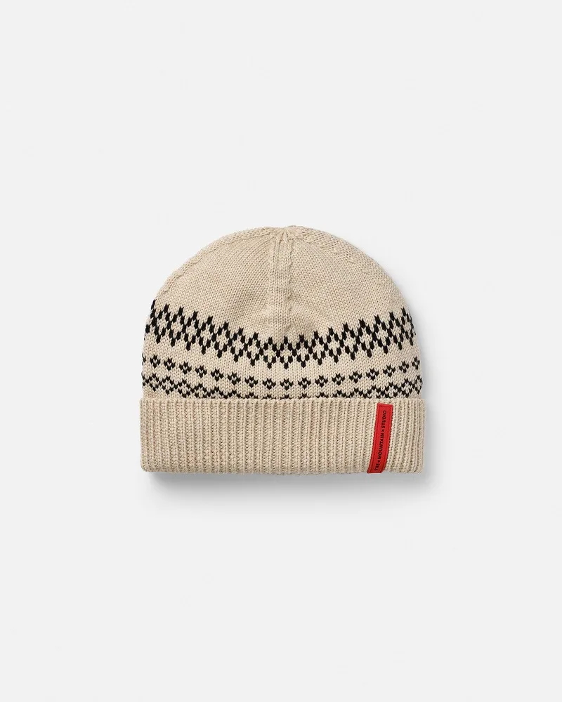 Bonnet en laine beige avec un motif jacquard noir et une étiquette logo rouge.