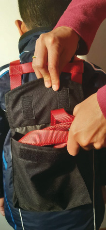 Pliage du sac de ski pour enfants Enfant avec entraîneur de ski : la corde rouge est rangée dans un sac noir sur le dos. Les mains des parents plient le sac.