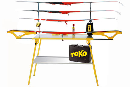 Gelber Servicetisch mit Ski, Ablageblech, Wachs, Werkzeug und Toko Tasche.