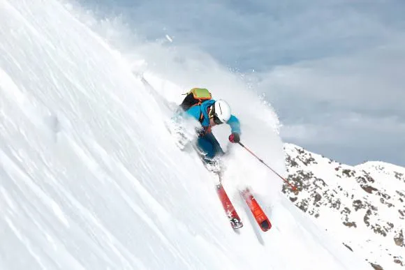 Ski tourer with Dynafit Hoji Free Ski in action, powder snow splashes, mountain landscape.