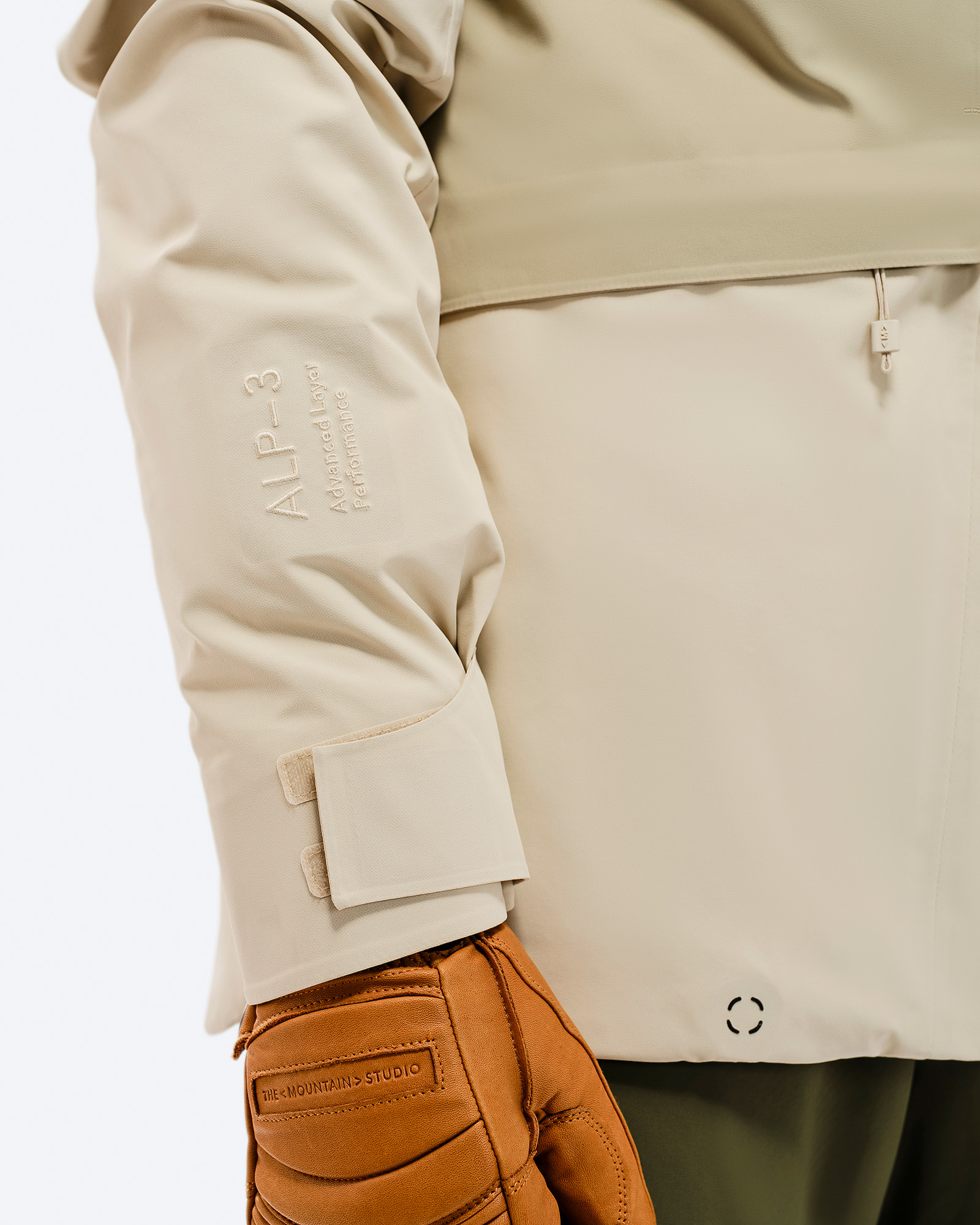 Beige Z-5 Hybridjacke Detailaufnahme der beigen Z-5 3L Hybrid Shell Jacket mit ALP-3 Logo am Ärmel und braunem Lederhandschuh.