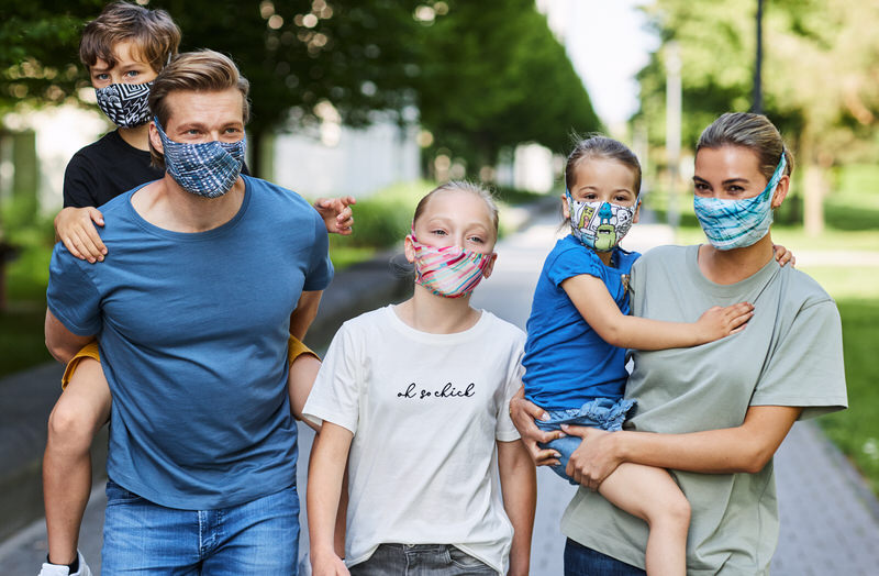 Familie mit Masken Familie trägt Masken. Sky Blue Maske ist bei der Frau vorne rechts zu sehen, Kind wird getragen.