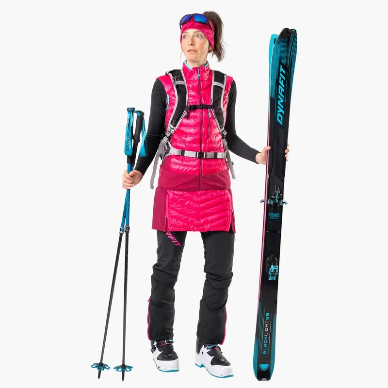 Frau mit Dynafit Blacklight 88 Ski, Skistöcken und Skitourenbekleidung vor einem weißen Hintergrund.