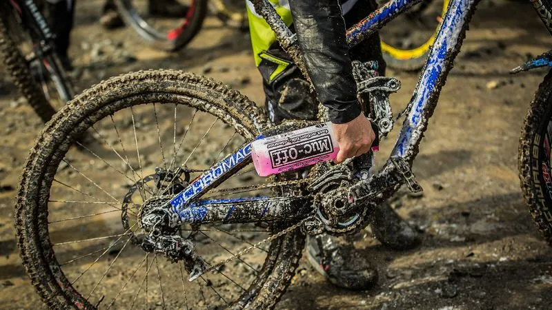 Schlammverschmutztes Fahrrad wird mit rosa Muc-Off Fahrradreiniger behandelt, Detailaufnahme.