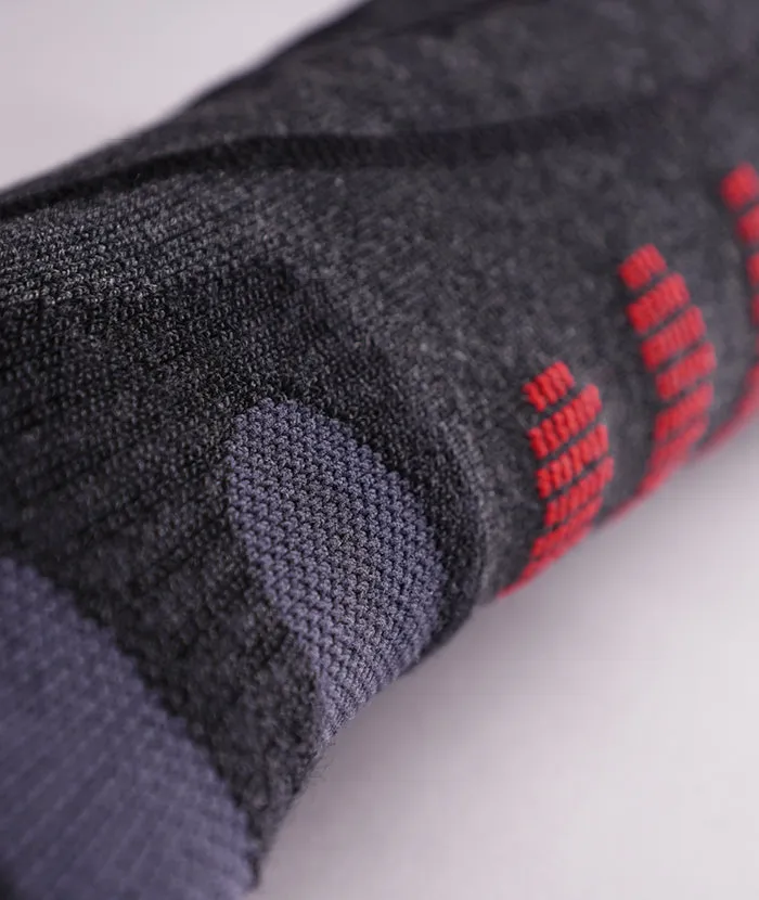 Gros plan sur une chaussette de laine grise roulée avec des accents rouges et un poignet gris foncé.