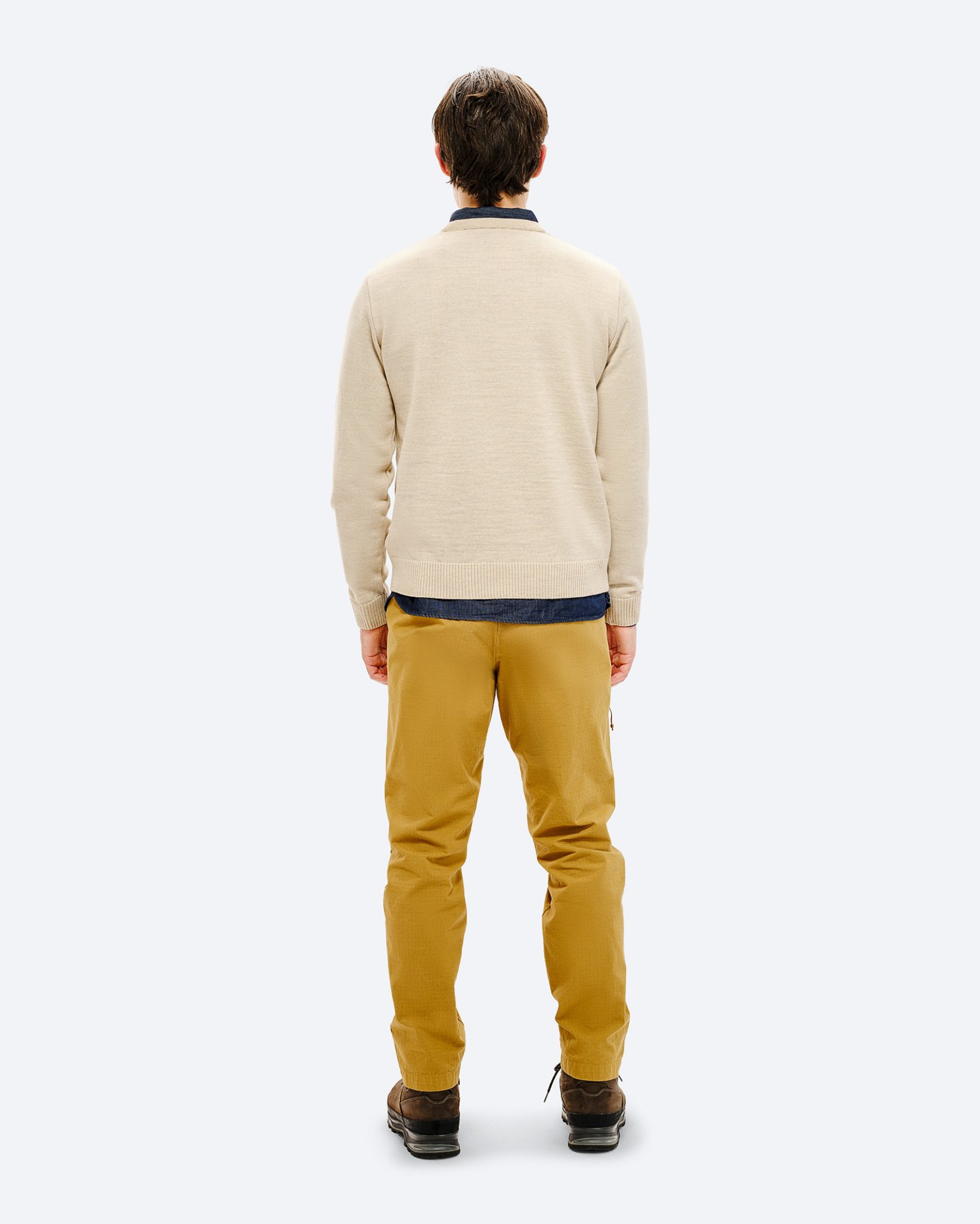 Man in ski outfit Rear view of a man wearing a beige ski sweater, yellow pants and brown shoes against a neutral background.