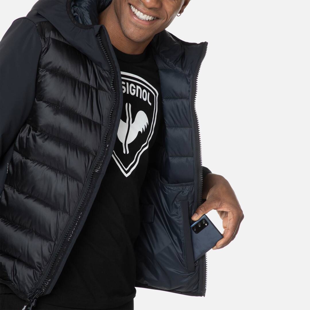 Rossignol Hoodie Schwarz Mann trägt Rossignol Stretch Quilt Hoodie JKT in Schwarz. Hand steckt Smartphone in die Jackentasche.