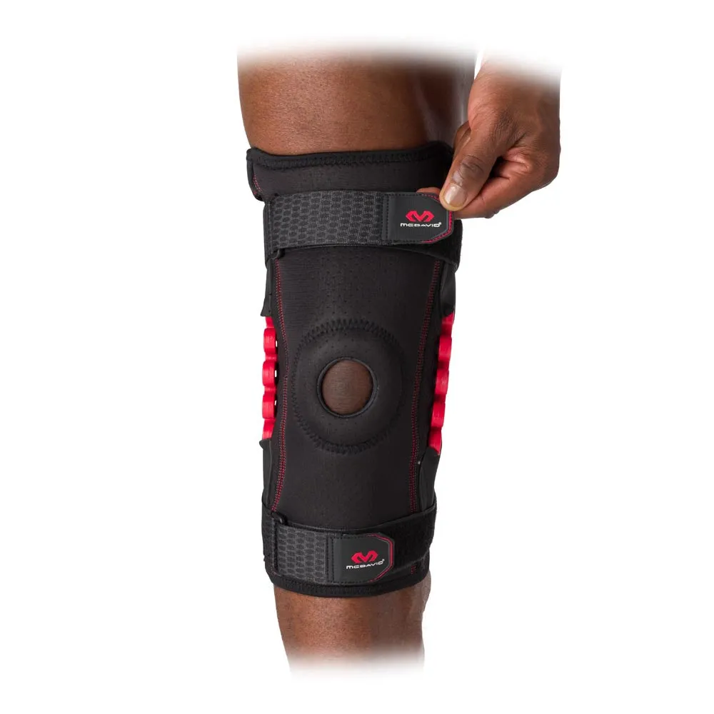 Close-up of a black MCDavid NRG Knee Brace on the knee, with red joint and hand on a strap.