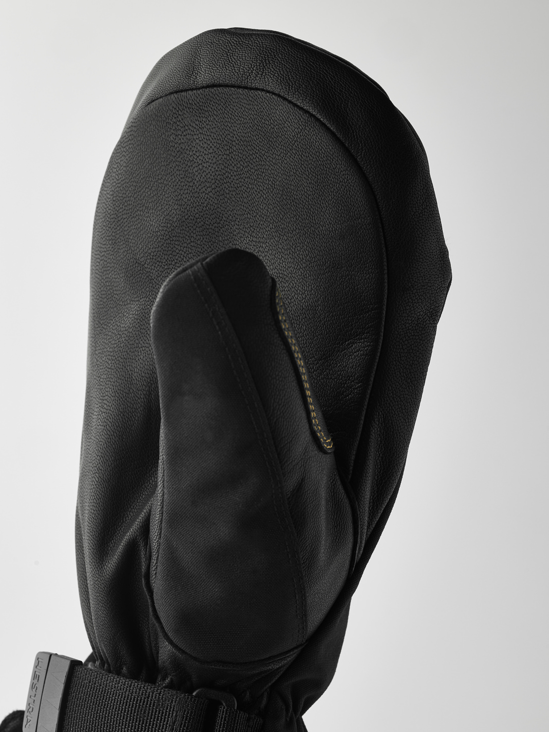 Gant en cuir noir Détail d'un gant en cuir noir avec le pouce, la manchette avec ruban et la boucle sur un fond clair.