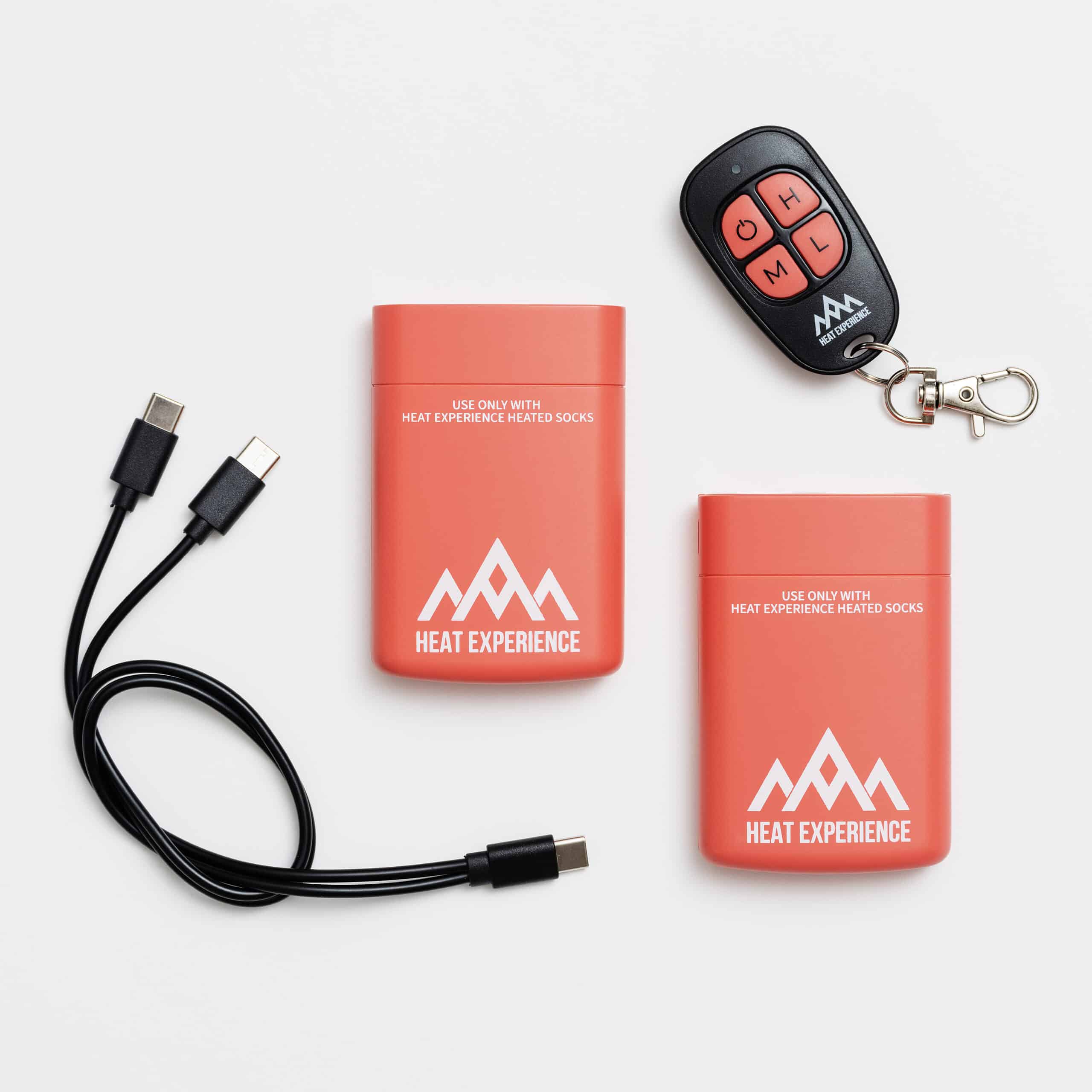 Zubehör für beheizbare Socken Zwei Akkus, USB-Kabel und Fernbedienung für Heat Experience beheizbare Skisocken auf weißem Grund.