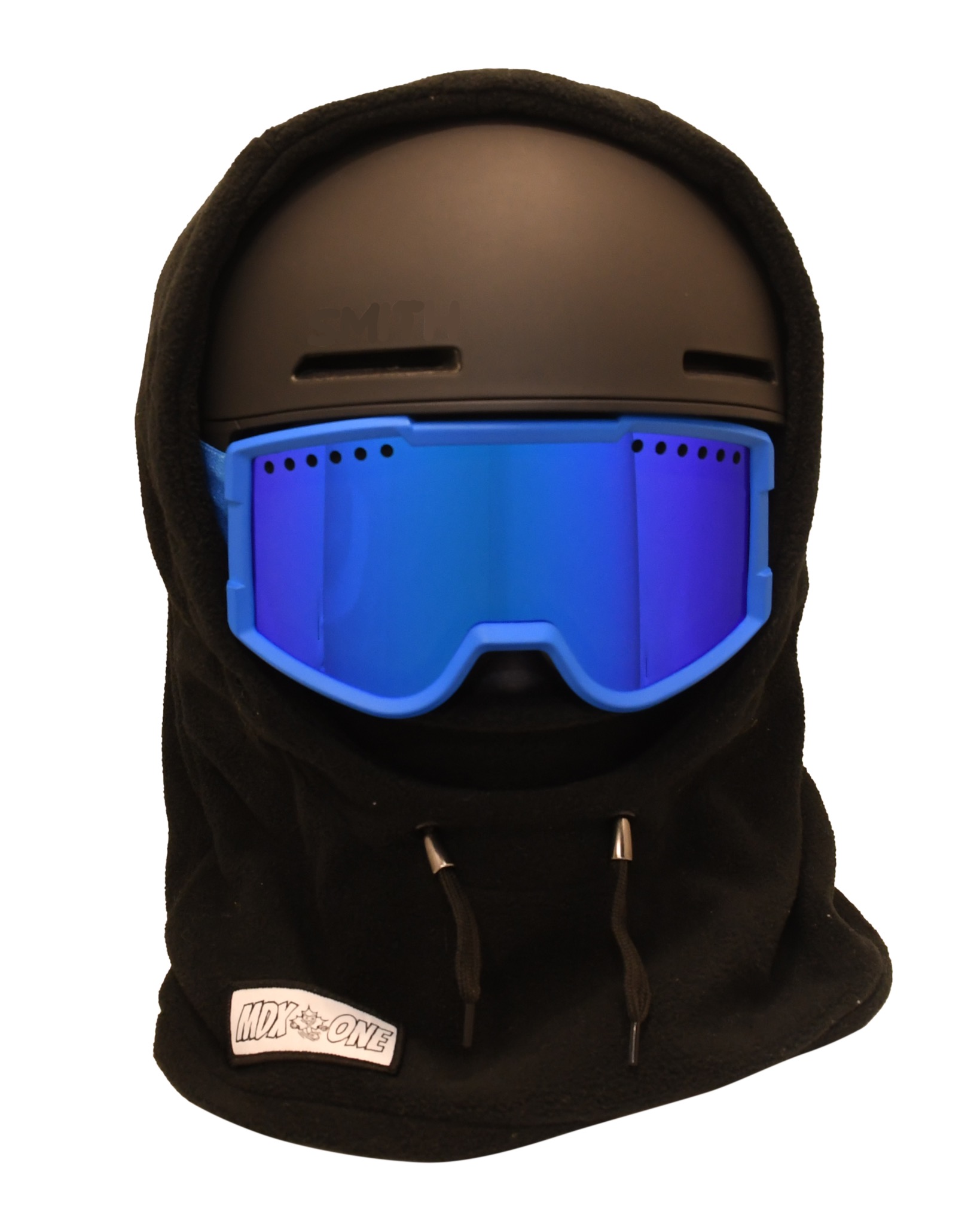 Cagoule noire enfant en polaire douce, portée sur casque de ski noir et lunettes bleues. Couvre tête, cou et visage pour protéger du froid, idéale ski et journées d'hiver. En bas à gauche : étiquette blanche « MDX-ONE ».