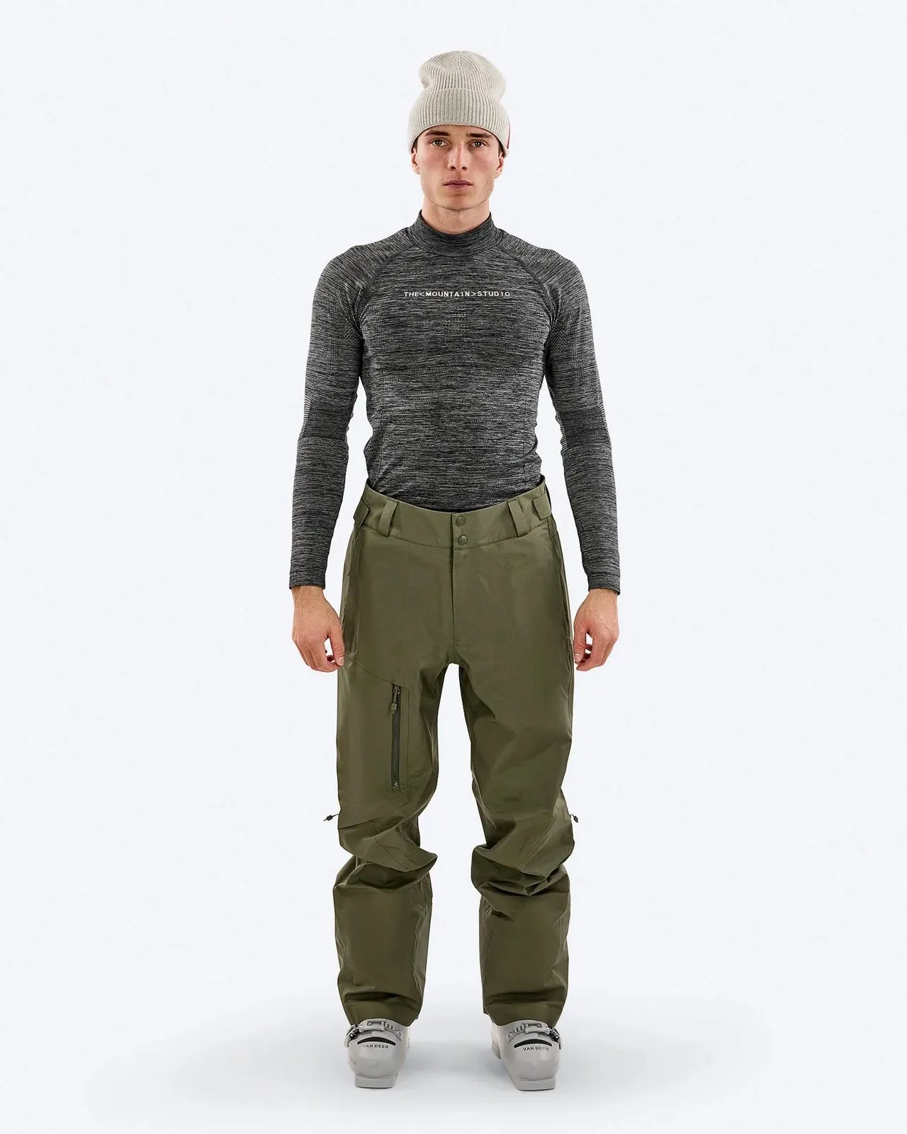 A man with a cap, long-sleeved top and ski pants stands in front of a white background.
