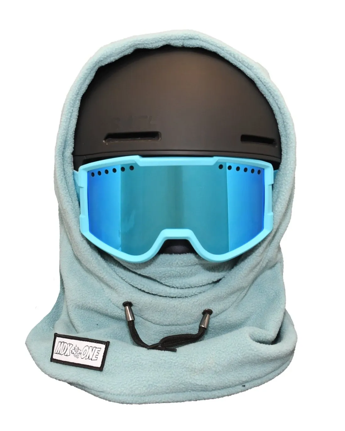 Teal-blue balaclava in soft polar fleece, covering a black ski helmet and extending over neck and face. Blue ski goggles with a light blue frame on top. Helmet-compatible balaclava for children, for cold protection. MDX ONE label visible.