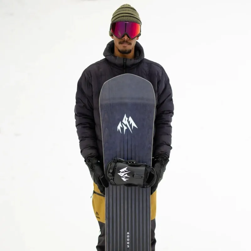 Person hält ein Jones Freecarver Snowboard mit Bindung vor sich. Er trägt Mütze, Skibrille, Jacke und Handschuhe.