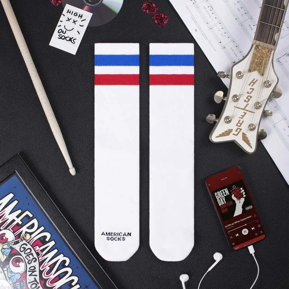Zwei weiße Mid High Socken mit blau-roten Streifen neben Schlagzeugstock, Gitarre und Smartphone.