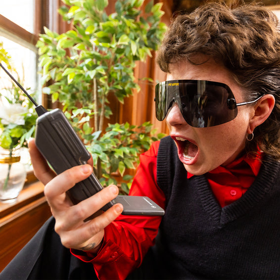 Person mit polarisierter Sonnenbrille hält ein altes Handy und schreit.
