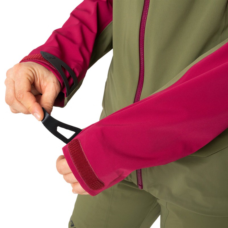Gros plan : une personne ajuste les manches d'une veste hybride rouge et verte Dynafit Beast pour femme. Focus sur les détails et la coupe.
