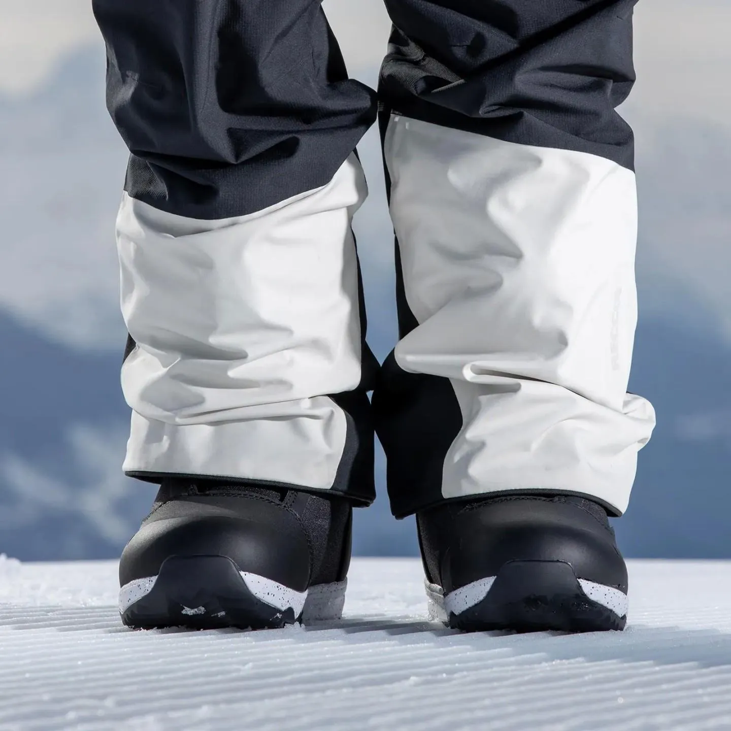 Jambes avec des chaussures de snowboard sur la neige. Jambes de pantalon en partie blanches enfilées sur les chaussures noires Nidecker Rift W.