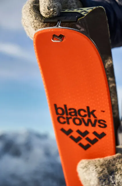 Vista dettagliata del terminale dello sci Draco Freebird di Black Crows di colore arancione con attacco per la pelle, tenuto da mani guantate.