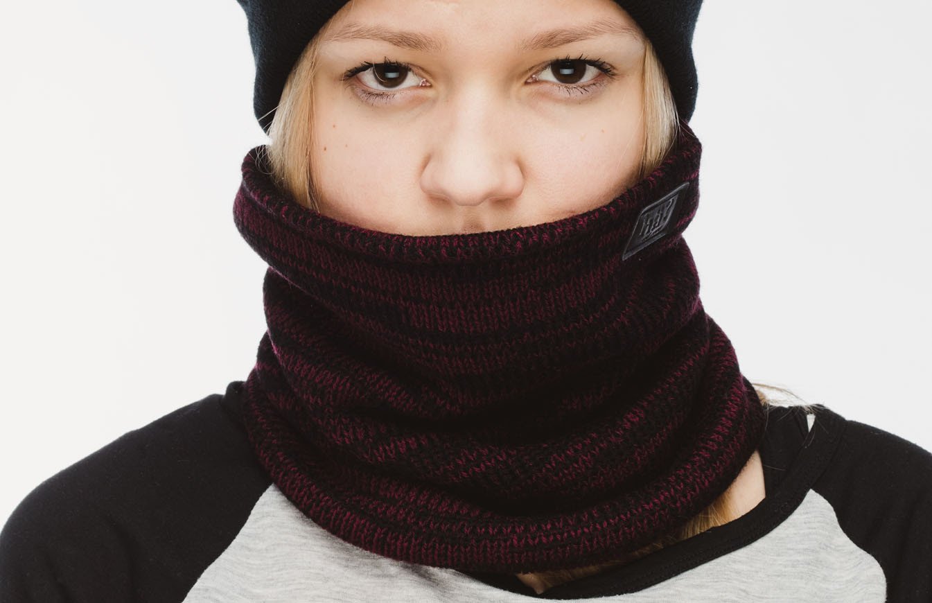 Porträt einer Person mit bordeauxfarbenem Melange-Neckwarmer, der bis zur Nase hochgezogen ist, und einer schwarzen Mütze.