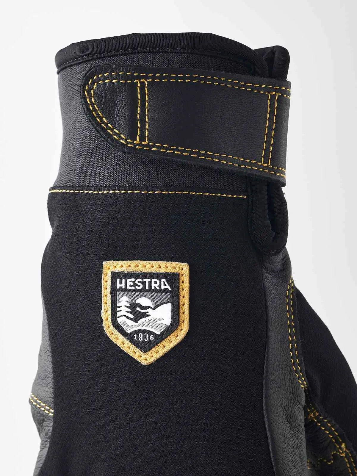 Detailaufnahme eines schwarzen Hestra Ergo Grip Active Handschuhs mit gelben Nähten und Markenlogo.