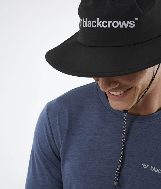 Ein Mann mit Black Crows Boonus Hat, schwarzer Stoffhut mit breiter Krempe und Kordel.