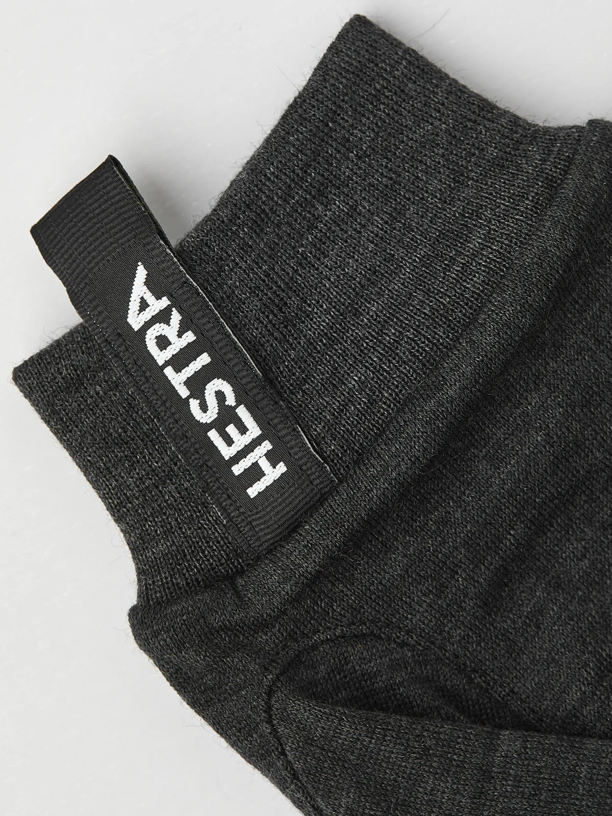 Primo piano di un guanto grigio in lana merino Liner Active con il logo Hestra sul polsino.