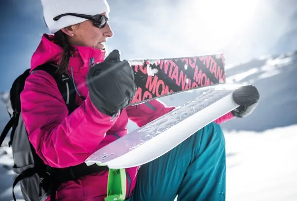 Woman holding Crossblades Hardboot snowshoes, mountain landscape in the background.