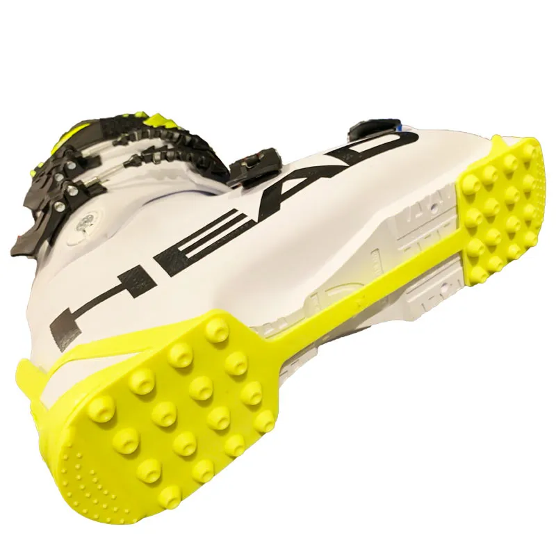White ski boot with yellow Cat Tracks sole cover showing spikes for better grip.