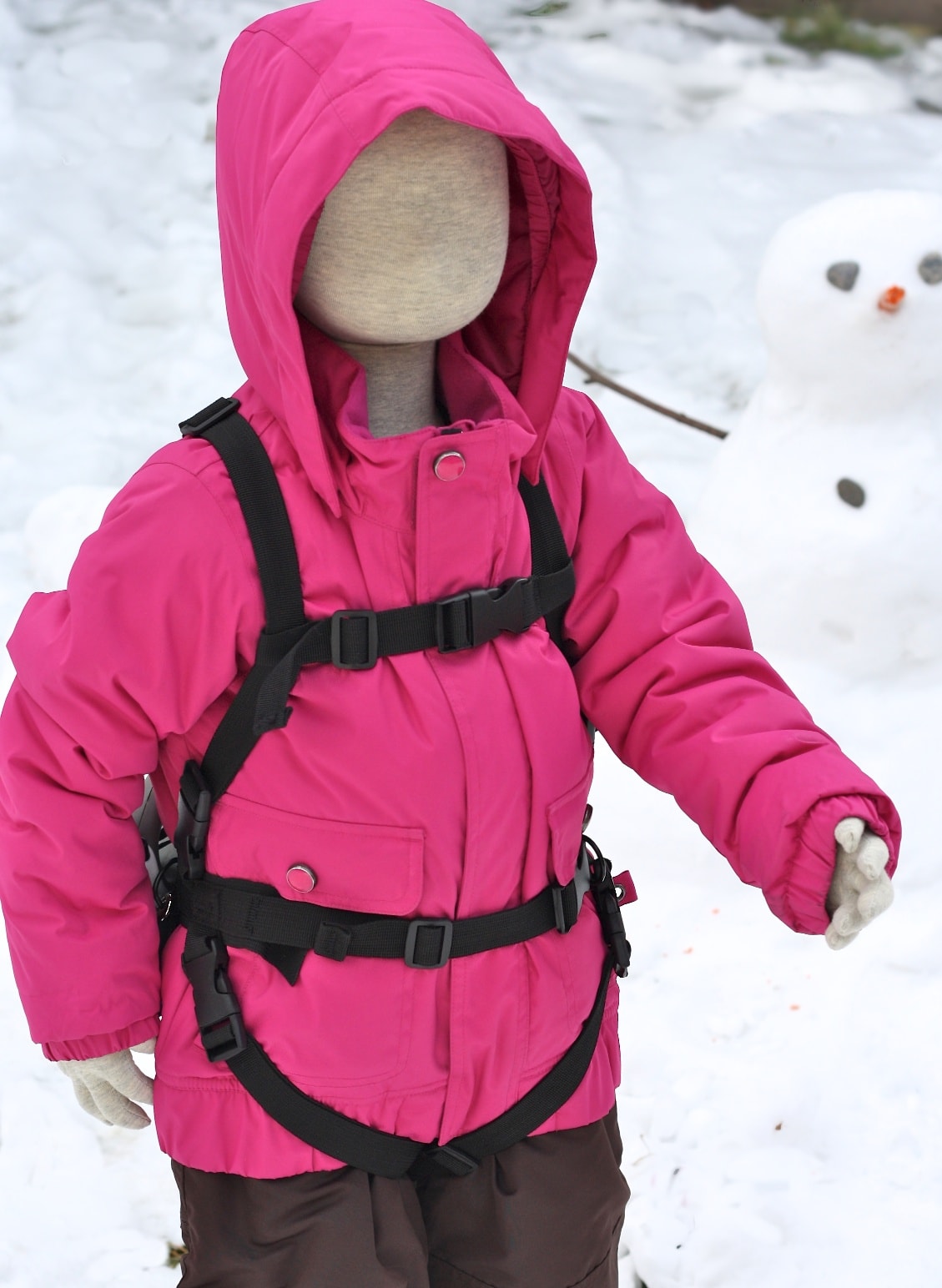 Poupée portant une veste d'hiver rose avec Lil' Ripper Gripper aide au ski dans la neige, en arrière-plan un bonhomme de neige.