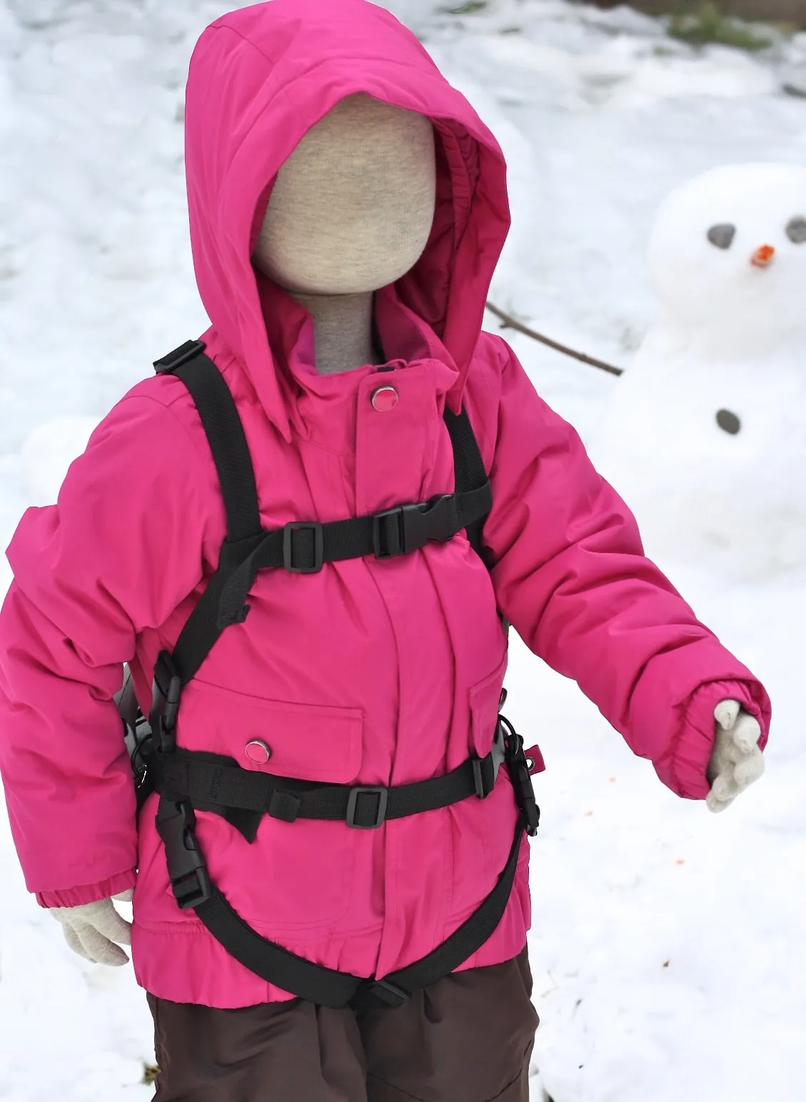 Poupée portant une veste d'hiver rose avec Lil' Ripper Gripper aide au ski dans la neige, en arrière-plan un bonhomme de neige.