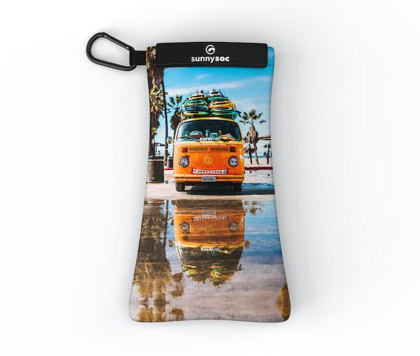 Sunnysoc mit einem gelben VW-Bus mit Surfbrettern auf dem Dach. Palmen und eine Strand Szene im Hintergrund.
