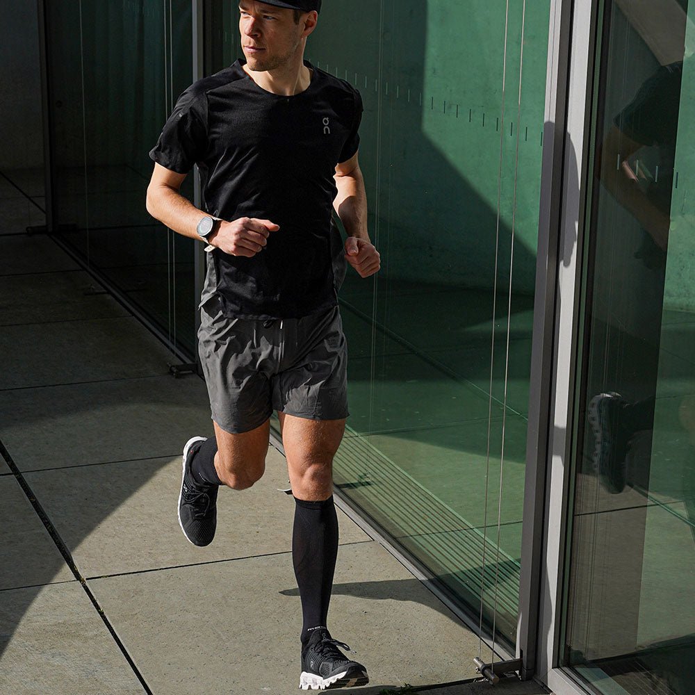 Läufer mit McDavid Elite Recovery Kompressionssocken, schwarzen Laufschuhen, Shorts und T-Shirt beim Laufen.