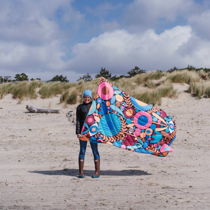 Person am Strand hält Rumpl Puffy Blanket Night Garden mit Blumenmuster.