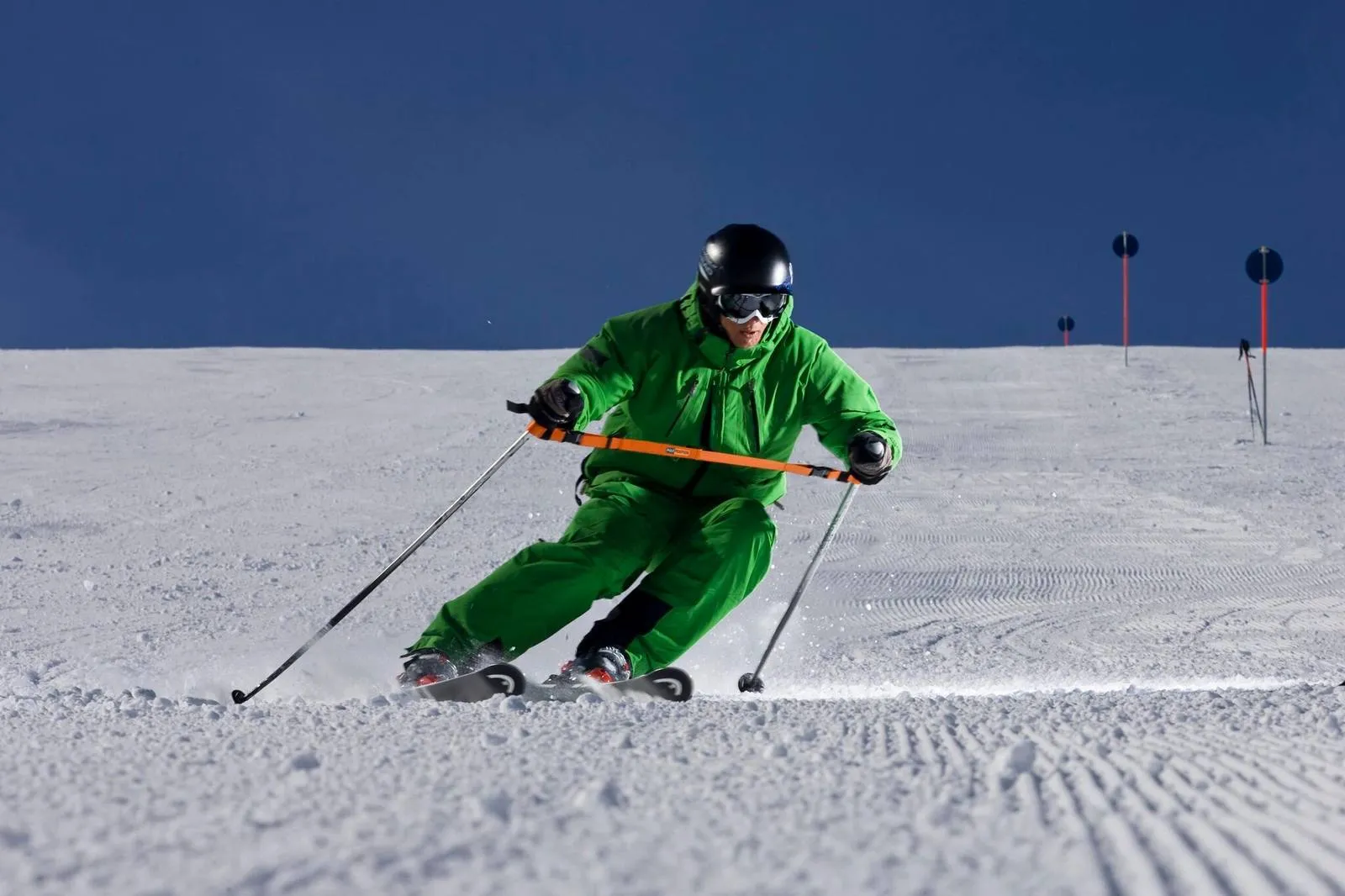 Skier in green clothing with training strap on a groomed slope.