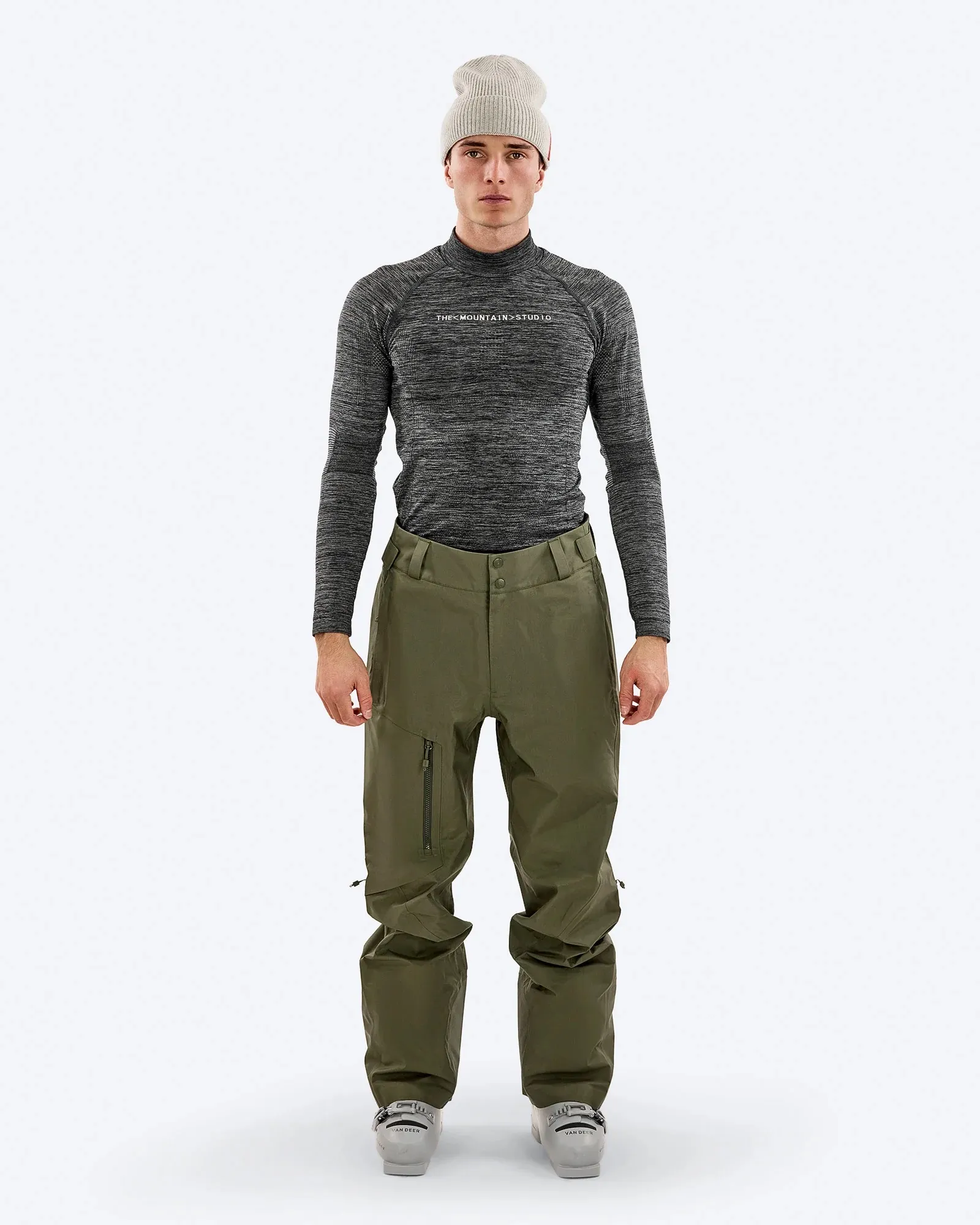 Un uomo con berretto, top a maniche lunghe e pantaloni da sci è in piedi davanti a uno sfondo bianco.