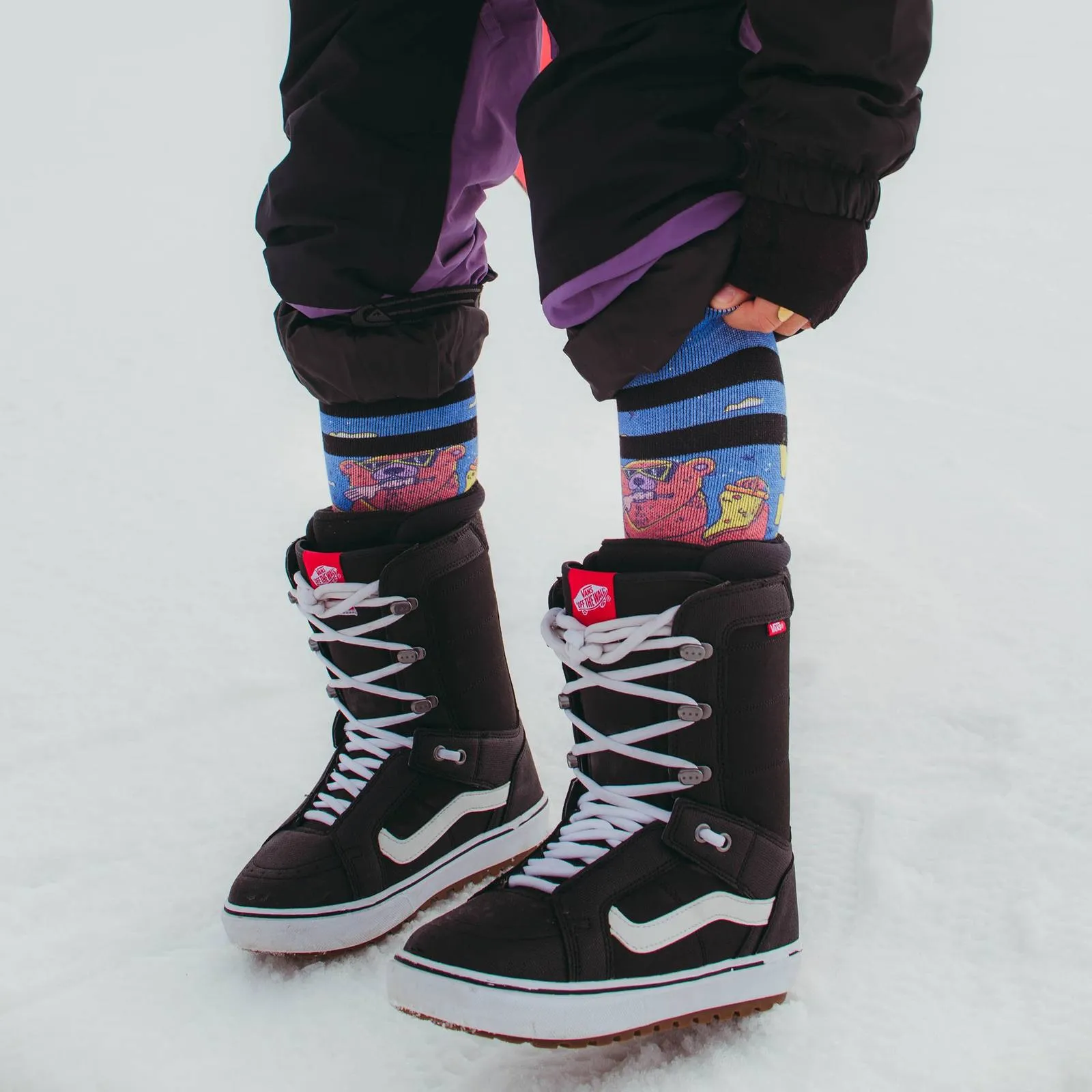 Persona con scarponi da snowboard e calzini Wild Nature sulla neve. Calzini con motivo di orso.