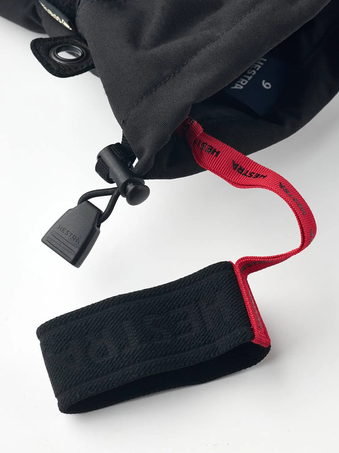 Close-up of a black Hestra Gore-Tex five-finger glove with red strap and black fastener.