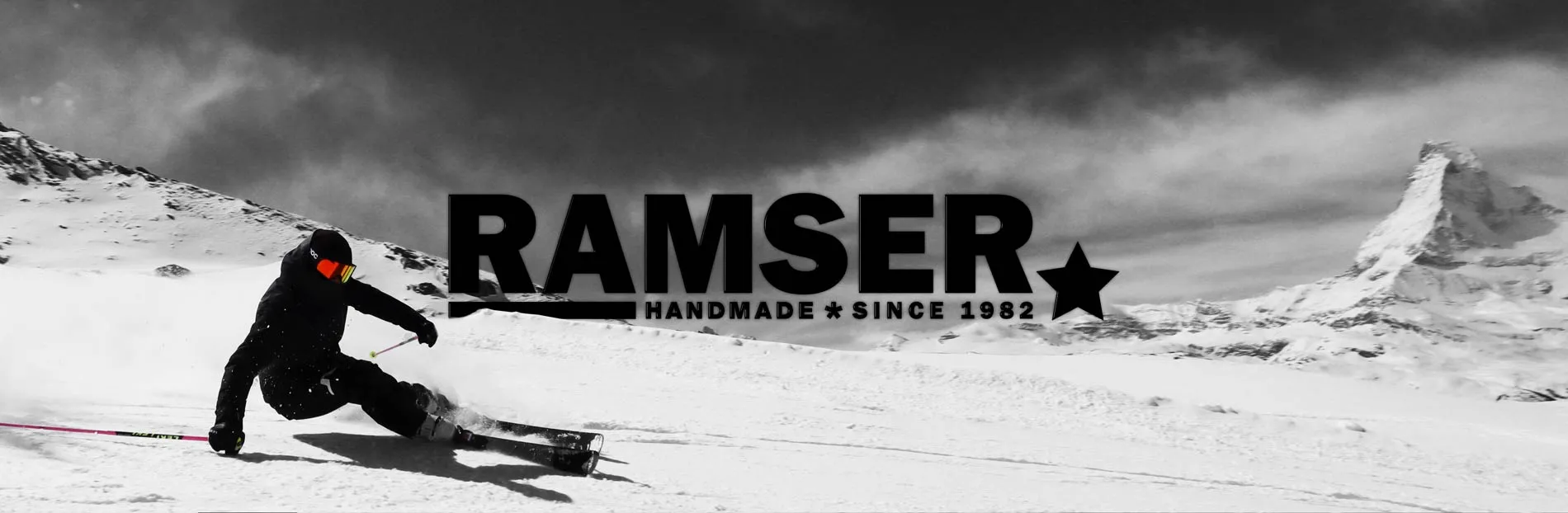 Skifahrer vor verschneiter Berglandschaft mit dem Schriftzug "RAMSER HANDMADE * SINCE 1982" im Zentrum des Bildes.