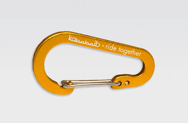 Detailansicht: Oranger kommit Karabiner mit silbernem Verschluss und weißer Aufschrift "kommit - ride together".