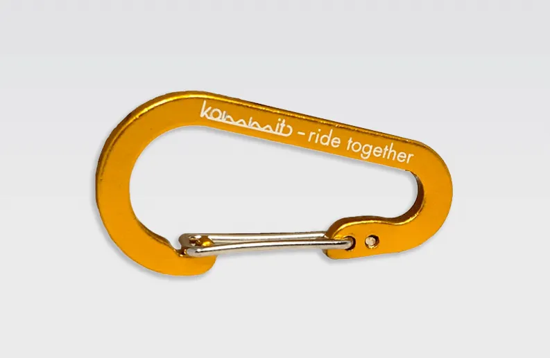 Detailed view: Orange kommit carabiner with silver clasp and white inscription "kommit - ride together".