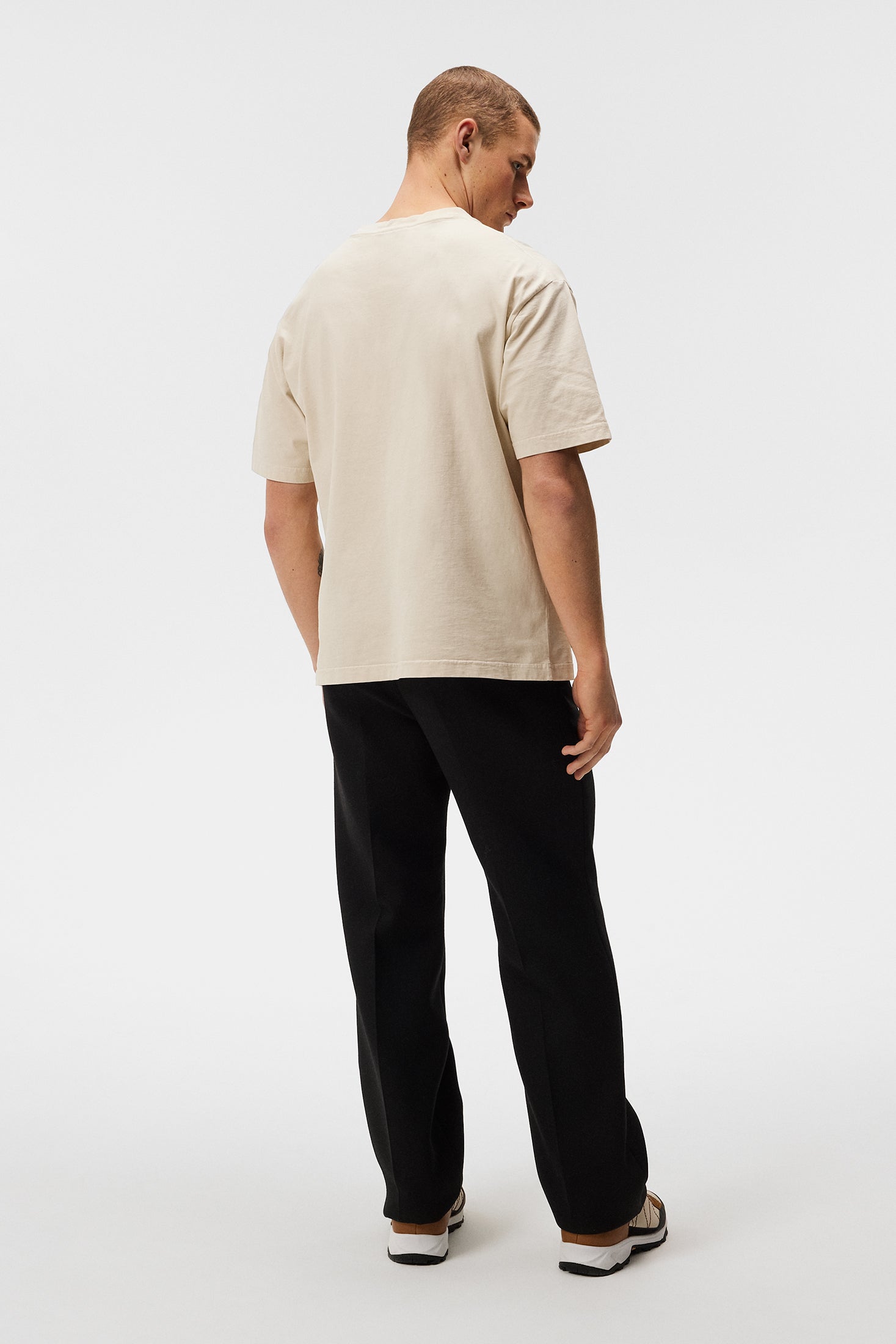 Teeau Oyster Gray Boxy Un homme porte un tee-shirt Oyster Gray Walsh Boxy Print, combiné à un pantalon noir, de dos sur un fond blanc.