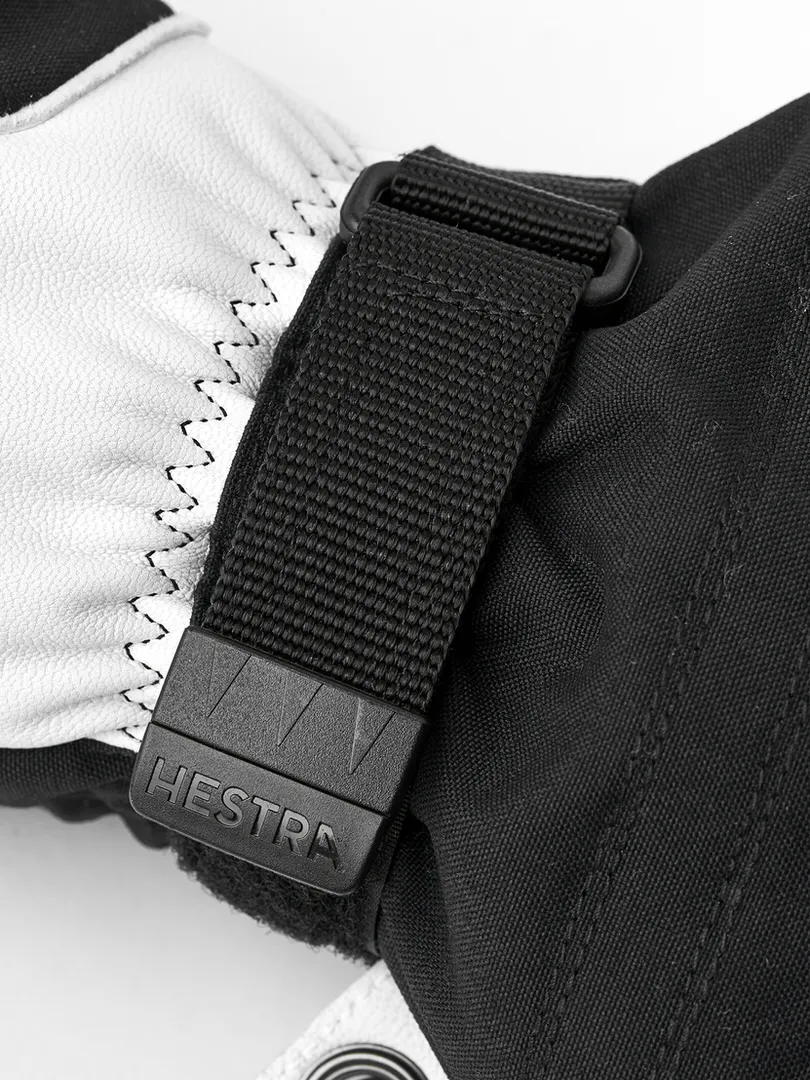 Détail d'un gant de ski noir Hestra avec une partie en cuir blanc et une sangle noire avec le logo Hestra.