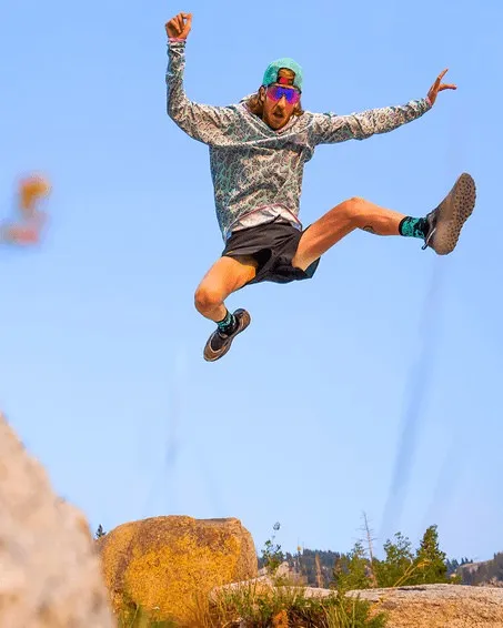 Uomo che salta con felpa e occhiali rosa davanti a un cielo blu.