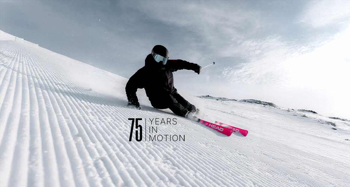 Skifahrer in schwarzer Kleidung auf einer präparierten Skipiste unter bewölktem Himmel.